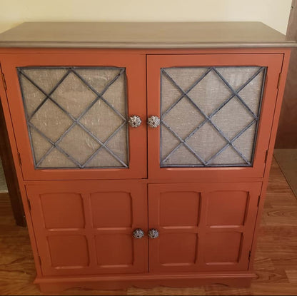 Orange cabinet with glass doors featuring diamond patterns on a wooden floor.