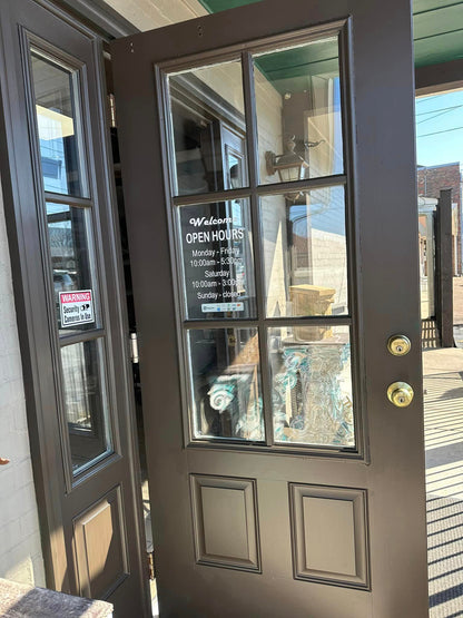 Brown door with glass panels and open hours sign, reflecting a building interior.